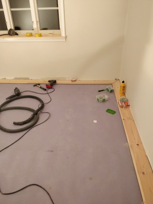 Golv under renovering med verktyg, bräder och golvyta redo för läggning av trägolv.