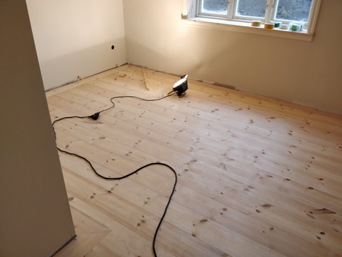 Omonterat massivt furugolv i ett rum med slipmaskin och elkabel på golvet.