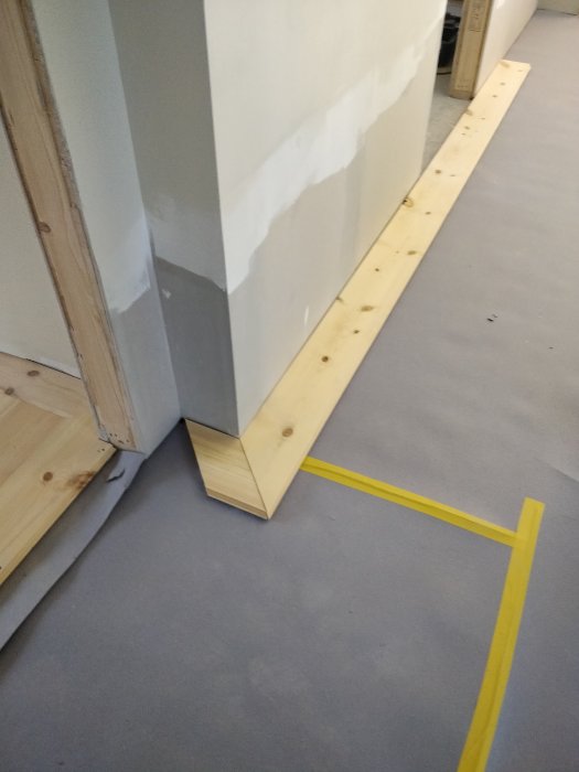 Delvis lagt furugolv med måttband och verktyg vid en vägghörna under renovering.