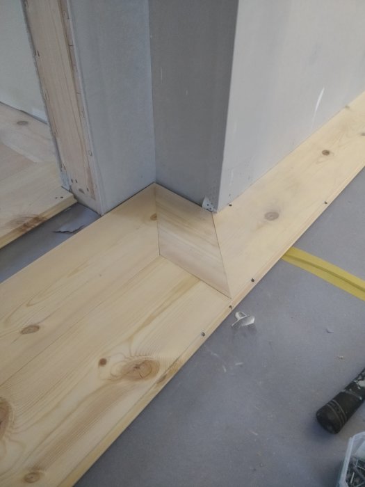 Installation av massivt furugolv med en fris runt karmen vid en vägg, verktyg och skruvar synliga på golvet.