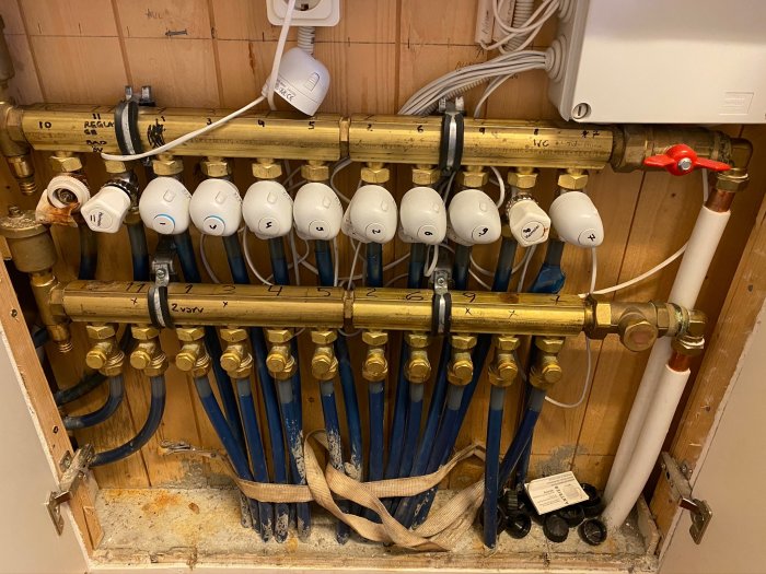 Värmesystem med märkta golvvärmeslingor och termostatventiler samt rör och en röd avstängningskran.