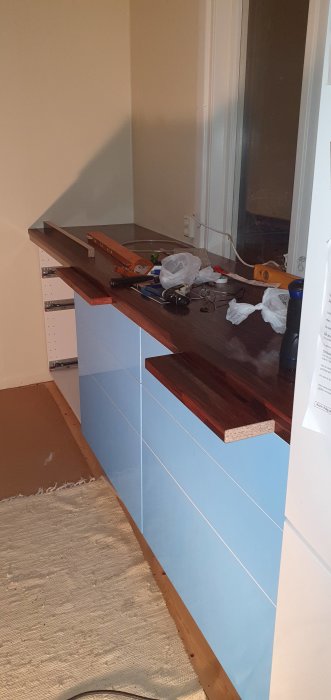 Kök under renovering med delvis installerad utdragbar skärbräda på mörk bänkskiva och verktyg.