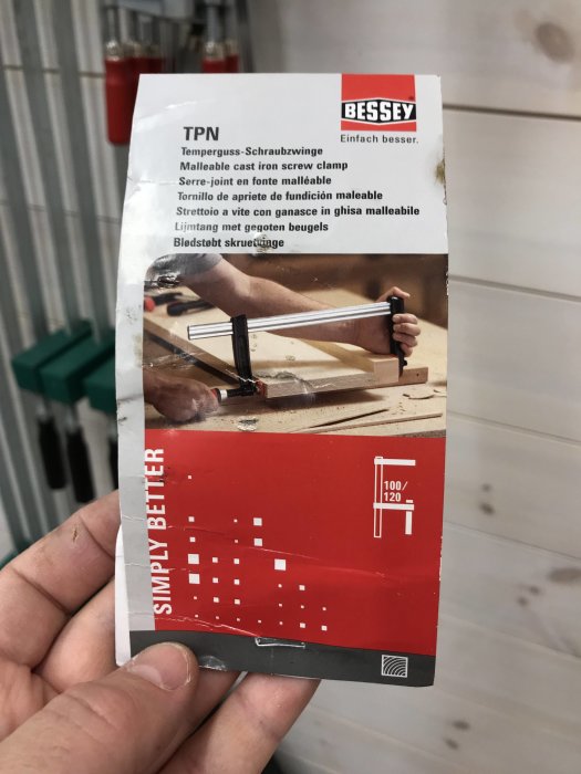 Hand som håller en Bessey-skrutvingförpackning med produktinformation och bild på användning.