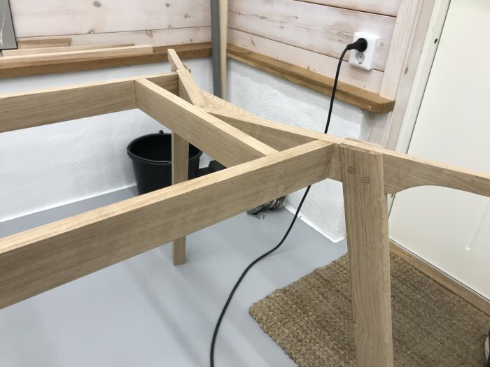Del av handtillverkat ekträbord med synliga pluggar och sammansatta benkonstruktioner i en verkstadsmiljö.