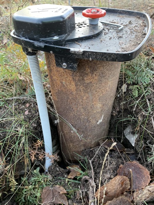 Brunnslock på brunnsrör i mark, utsatt för frost med angränsande ledning synlig.