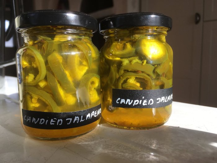 Två burkar med candied jalapeños, etiketterade, i solljus.