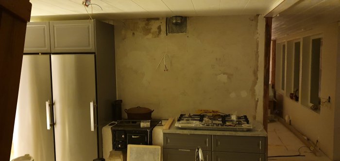 Kök under renovering med IKEA-skåp, kyl/frys, kakelugn och en borttagen gashäll.