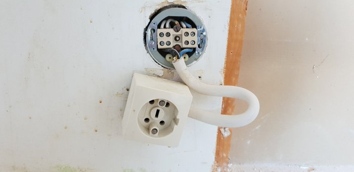 Elektrisk kabel med oansluten kontakt framför en öppen väggdosa.