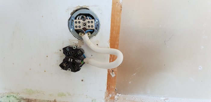 Elektrisk vägguttag med avkopplad kontakt och utdragna kablar under ett kökrenoveringsprojekt.