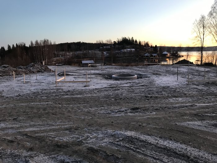 Frostig byggplats i gryningen med uppmätta områden för betongplatta, nära vatten.