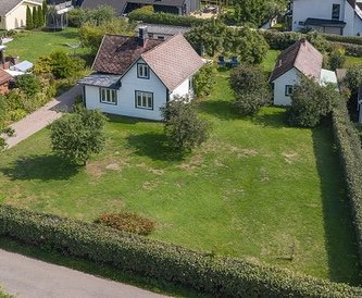 Drönarvy av en tomt med ett hus, potentiell byggyta ut mot vägen synlig.