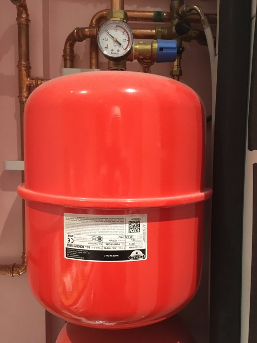 Röd expansionskärl för värmesystem med kopparledningar och tryckmätare som visar över noll.