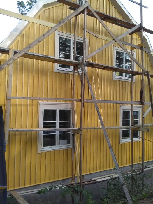 Renoverat 20-tals hus med gulfärgad fasad och nymontade foder runt fönstren.