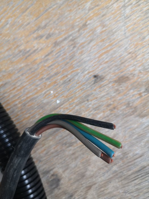 Elektrisk kabel med fyra oisolerade ledare utan foliemantel på träbakgrund.