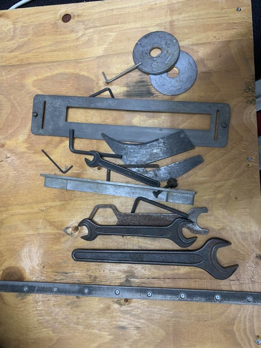 Uppsättning av mörkfärgade metallverktyg, inklusive skiftnycklar och tänger, som ligger på ett träbord.