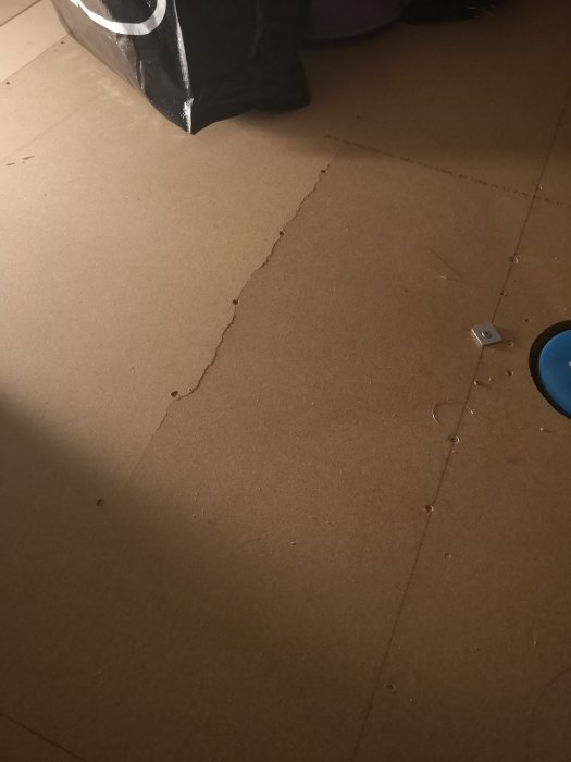 Spricka i en brun byggskiva på golvet i ett rum som indikerar potentiell skada relaterad till fall mot en brunn.