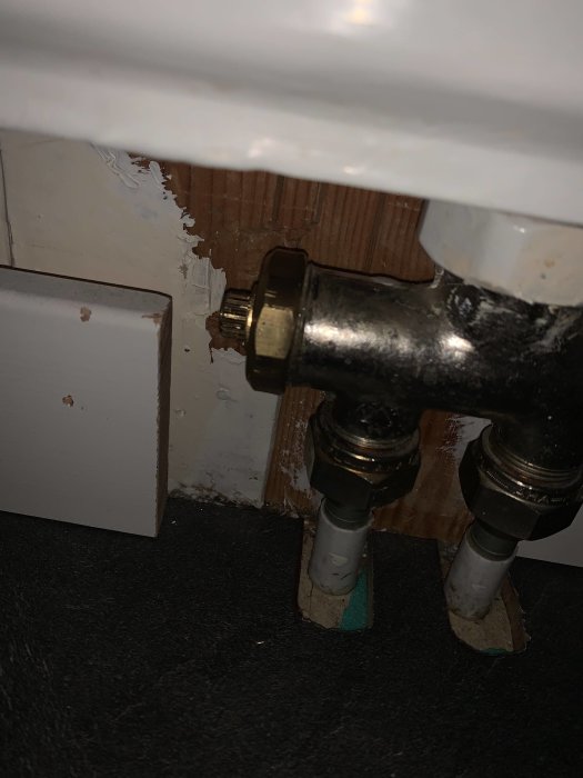 Mittkopplad radiator med öppen guldig ventil, synliga rör och flagande väggfärg.