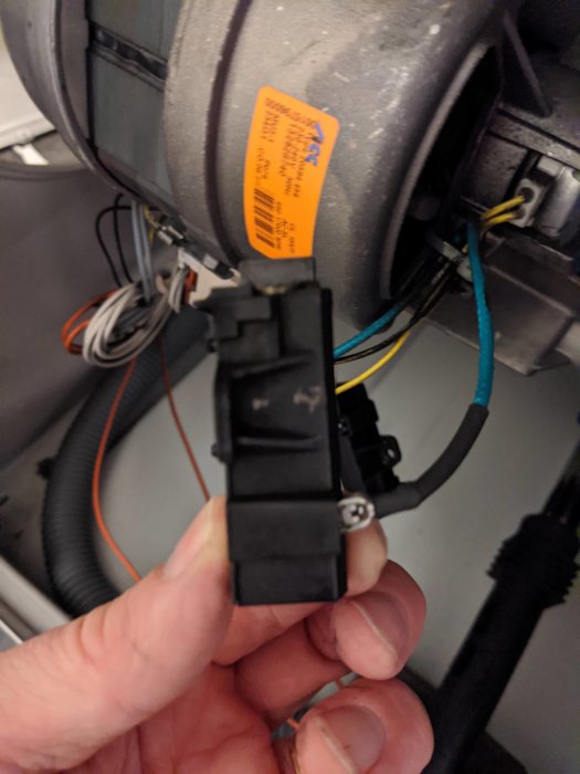 Hand håller en svart elektrisk hållare med kablar mot en motor.