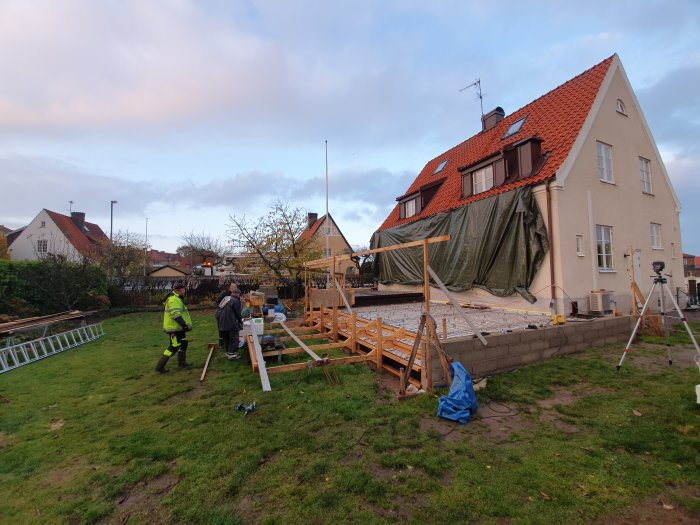 Arbetare förbereder för gjutning av grund vid byggplats med hjälp av armering och formar framför ett hus.