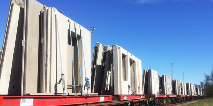 Prefabricerade betongväggelement med EPS isolering lastade på en tågvagn under en klarblå himmel.