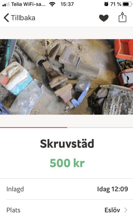 Begagnad skruvstäd ligger på ett smutsigt garagegolv omgiven av diverse verktyg och förpackningar.