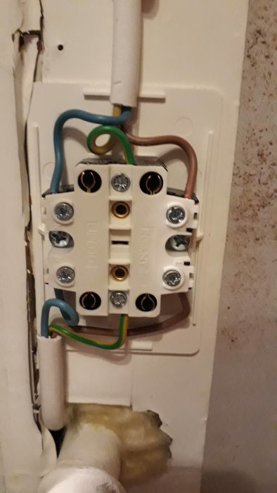 Öppet ojordat vägguttag med synlig jordtråd och anslutna kablar i ett uterum.