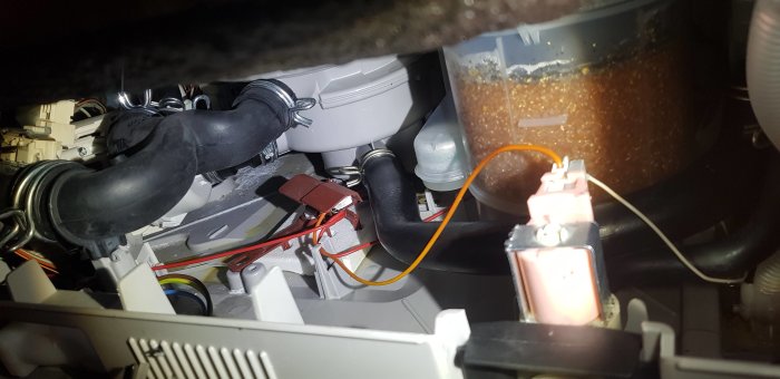 Interiör av en öppnad diskmaskin som visar rör, ledningar och komponenter, med tecken på läckage.