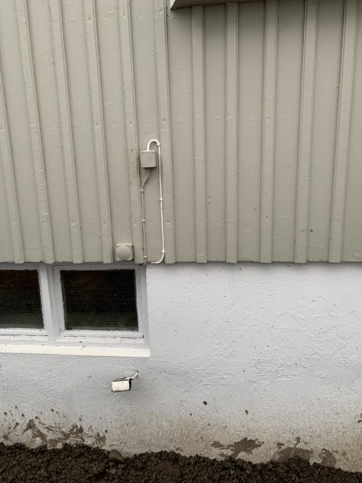 Oorganiserad kabeldragning på en husvägg med sprucket uttag och övermålad kabel.
