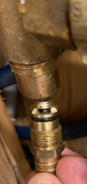 Närbild på en hand som håller en mässingsnippel med gängor, delvis urskruvad från en koppling.