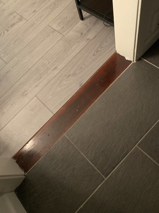 Nyinstallerat ljust trägolv möter äldre mörk tröskel bredvid grå klinkers.
