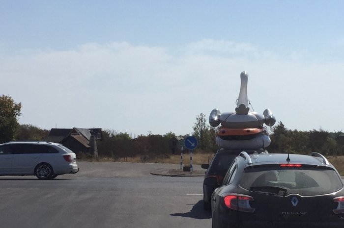 Bil parkerad med en uppblåsbar robotliknande figur på taket under solig himmel.