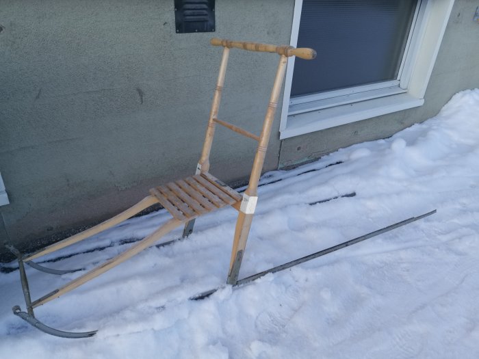 En sparkstötting lutad mot ett hus med snöig mark.