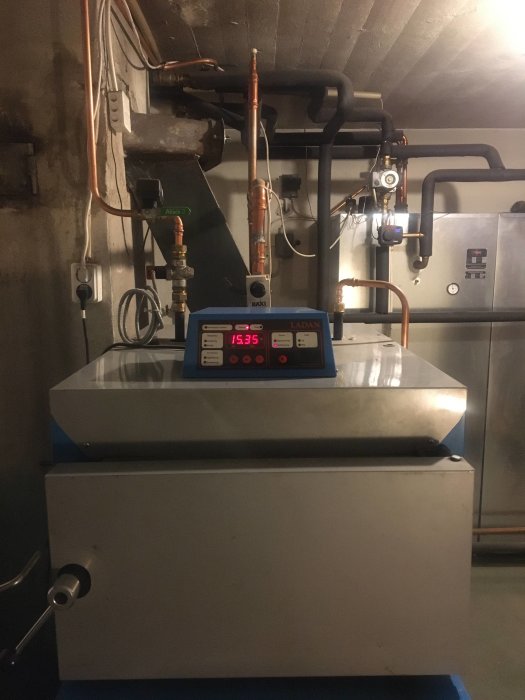 Vedpanna med laddomat och ackumulatortankar i ett pannrum, diverse rör och mätinstrument syns.