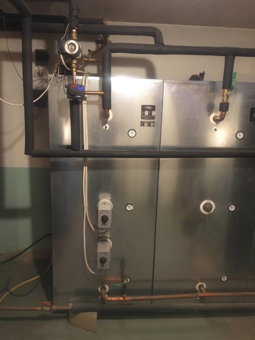 Vedpanna med laddomat och ackumulatortankar i ett pannrum, vissa rördelar i förgrunden.