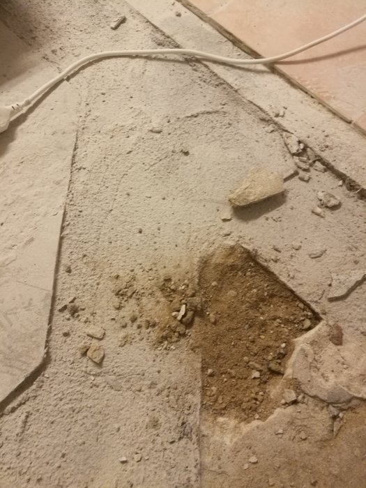 Källargolv med borttagen klinkers, betongplatta med synligt jordområde och sprickor, byggskada på hus från 1956.