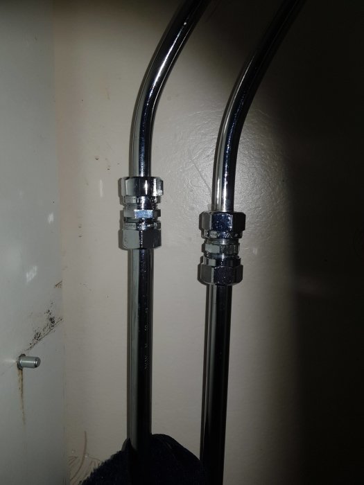 Två metallrör med kopplingar inne i ett mörkt skåp, upplyst med blixt, inga synliga sprickor.