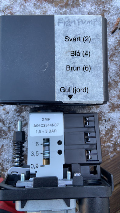 Tryckströmbrytare och etikett med ledningsinstruktioner, märkningar för Svar (2), Blå (4), Brun (6), och Gul (jord).