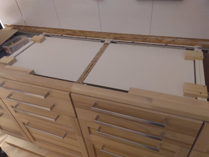 Nyinstallerad vit skiva på köksbänk med trästödbitar, över en rad av trälådor med metallhandtag.