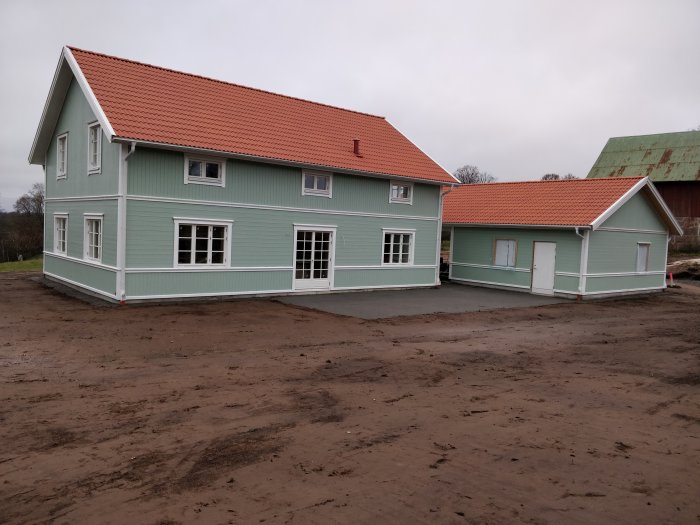 Nybyggd ljusgrön villa med carport, nylagd grusväg och återställd matjord runtomkring.