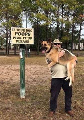 Man håller en stor hund framför skylt som instruerar att plocka upp hundbajs.