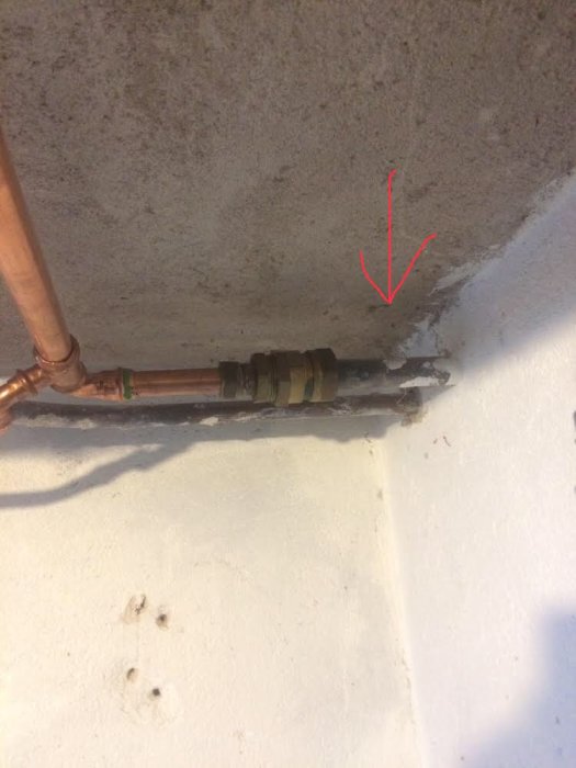 Vattenrör med tecken på rost och läckage uppmärksammat med röd pil på vägg och tak.