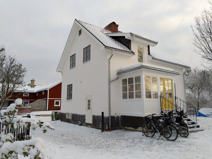 Vitkalkat hus i vinterskrud med snö på marken och cyklar parkerade framför.