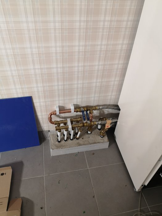 Installation av rörledningar ordnade på rad med kopplingar och ventil på betongplatta vid vägg.