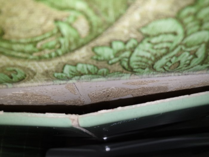 Grönt löst kakel vid kanten av ett badkar med synlig underliggande väggstruktur.