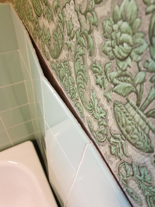 Grönt vintage kakel bredvid tapet i ett badrum med en spricka i fogningen