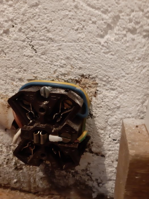 Öppen eluttag utan täckplatta, exponerade kablar och kontakter på en råputsad vägg.