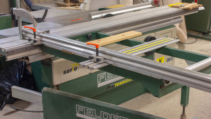 Justersåg i verkstad med tillbehör som klyvanhåll och justerbart anhåll, skydd och utsug synligt.