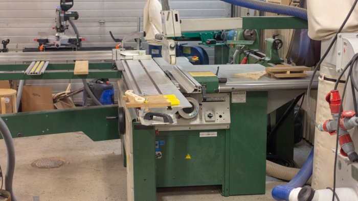 Robust justersåg i verkstad med skydd, utsug och anhåll, samt verktyg och trämaterial i närheten.