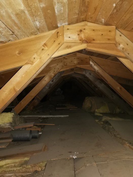 Attic space with wooden rafters and insulation material, preparations for construction work visible.