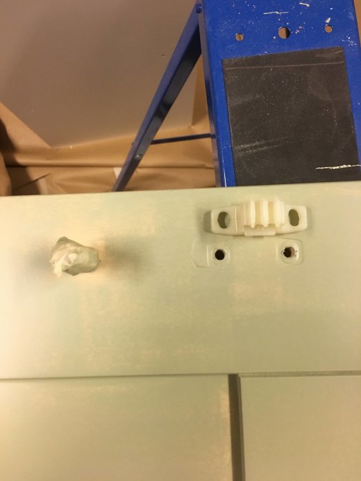 Nyfärgad kökslucka med plastbeslag och en synlig skruv, mot bakgrund av blå stege.